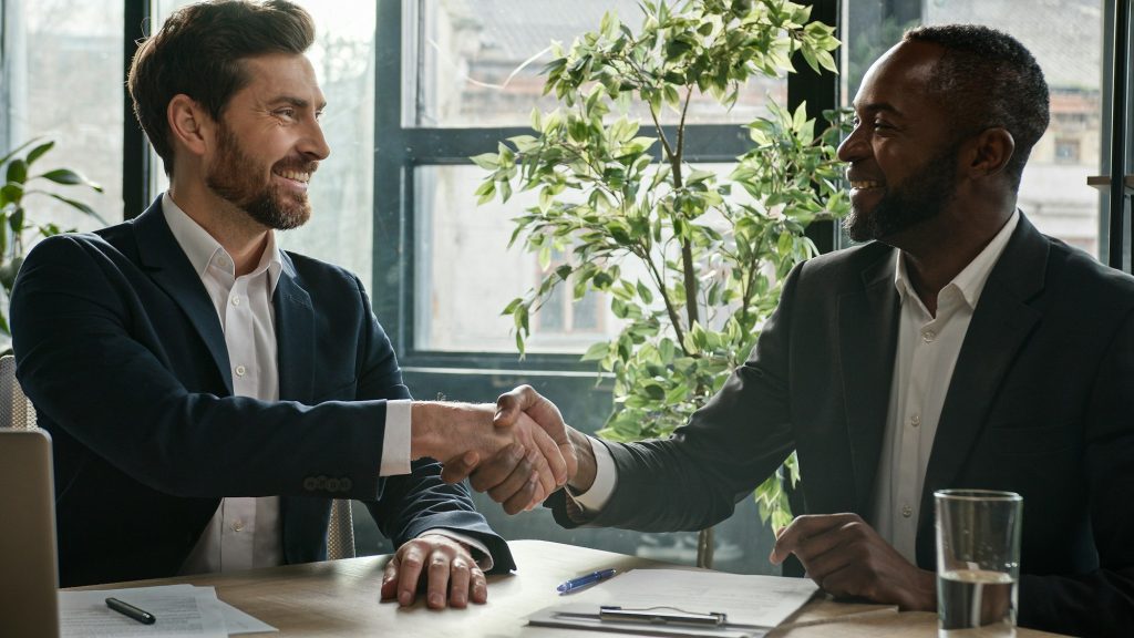 Two diverse multiracial businessmen signing document agreement shaking hands success business deal